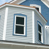 A house exterior with light gray siding and blue trim around two white-framed 10% VLT static cling tinted window, beneath a section of blue fish-scale shingles.