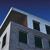 Modern building with gray bricks and metallic facade under a blue sky.